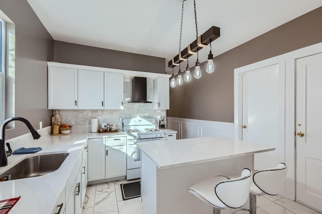 kitchen featuring wall chimney exhaust hood, sink, decorative light fixtures, white range oven, and white cabinets