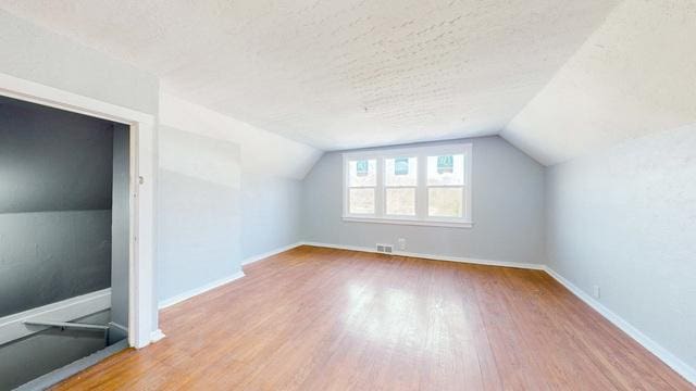 bonus room with hardwood / wood-style floors, lofted ceiling, and a textured ceiling