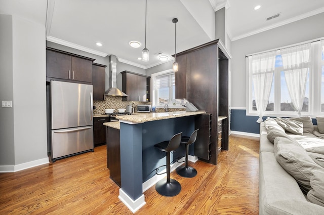 kitchen featuring appliances with stainless steel finishes, hanging light fixtures, a kitchen breakfast bar, dark brown cabinetry, and wall chimney exhaust hood