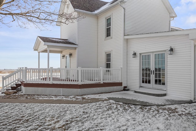 snow covered house featuring french doors, a shingled roof, and a deck