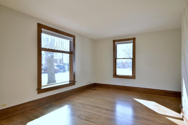 empty room with baseboards, wood finished floors, visible vents, and a healthy amount of sunlight