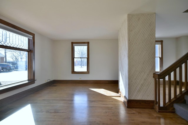 empty room featuring wood finished floors, visible vents, baseboards, and stairs