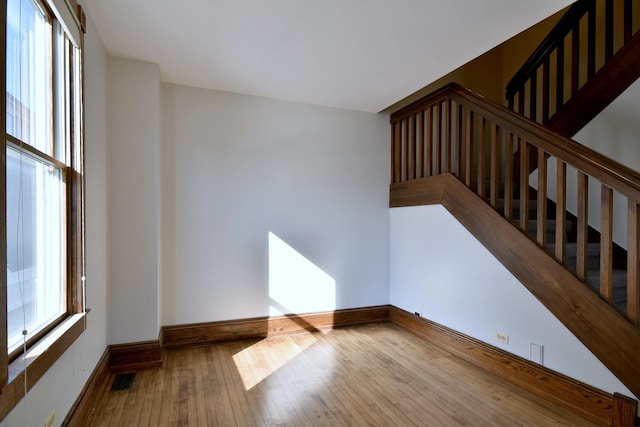 unfurnished room featuring hardwood / wood-style flooring, baseboards, stairs, and visible vents