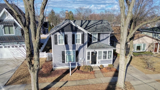 traditional-style home featuring concrete driveway, roof with shingles, fence, and a chimney