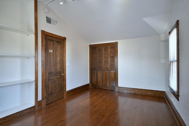 unfurnished bedroom with lofted ceiling, visible vents, baseboards, and wood finished floors