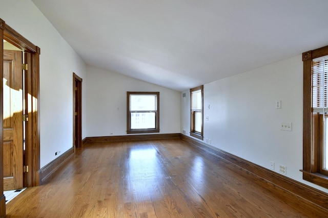 empty room featuring lofted ceiling, visible vents, baseboards, and wood finished floors