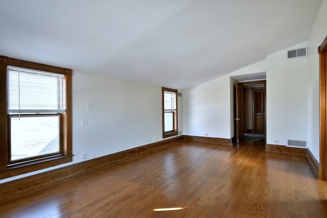 empty room with lofted ceiling, visible vents, baseboards, and wood finished floors