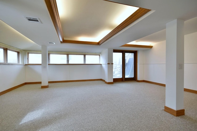 carpeted empty room with visible vents, a raised ceiling, and wainscoting