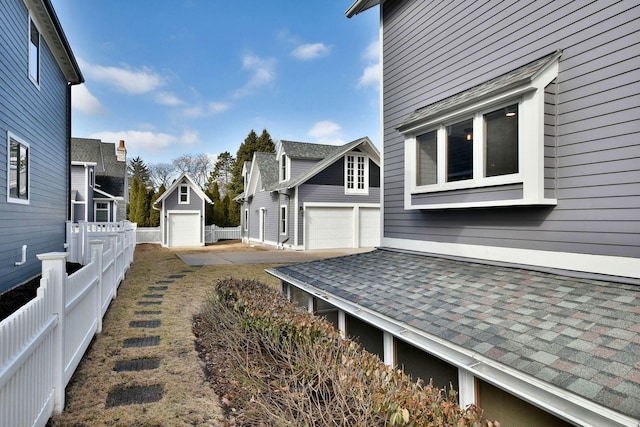 view of side of property featuring roof with shingles, an outdoor structure, and fence