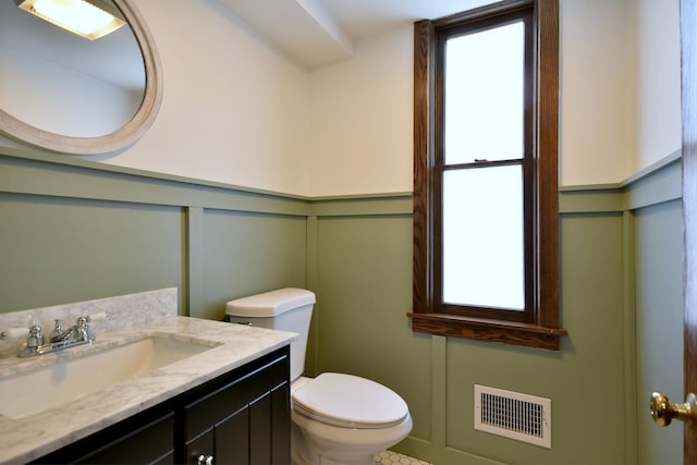 half bath with toilet, a decorative wall, vanity, visible vents, and a wealth of natural light