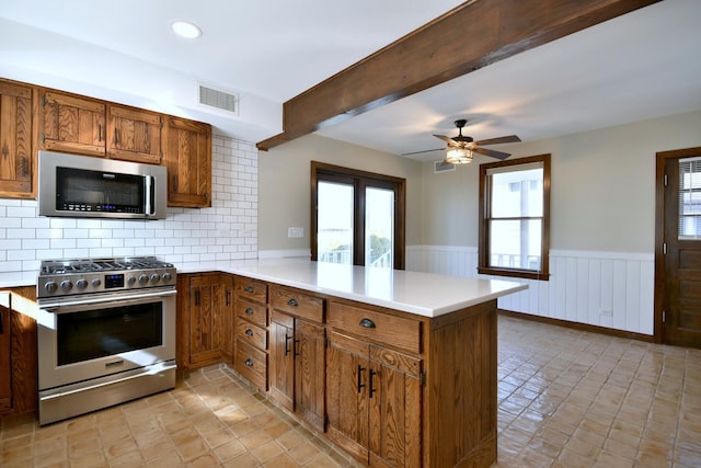 kitchen featuring a wainscoted wall, a peninsula, appliances with stainless steel finishes, and a healthy amount of sunlight