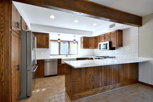 kitchen featuring stainless steel appliances, a peninsula, a sink, visible vents, and brown cabinetry