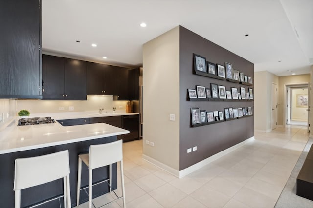 kitchen featuring sink, light tile patterned floors, a breakfast bar area, kitchen peninsula, and stainless steel gas stovetop