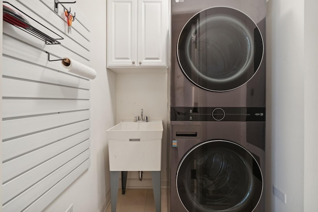 laundry area with tile patterned flooring, sink, cabinets, and stacked washing maching and dryer