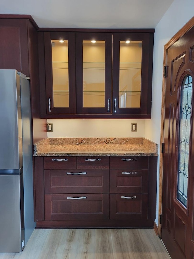 bar featuring light stone counters, dark brown cabinets, stainless steel fridge, and light hardwood / wood-style flooring