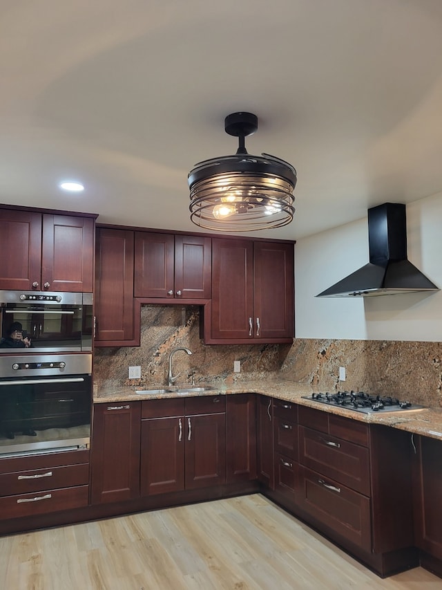 kitchen featuring sink, extractor fan, stainless steel gas stovetop, light stone countertops, and light hardwood / wood-style floors