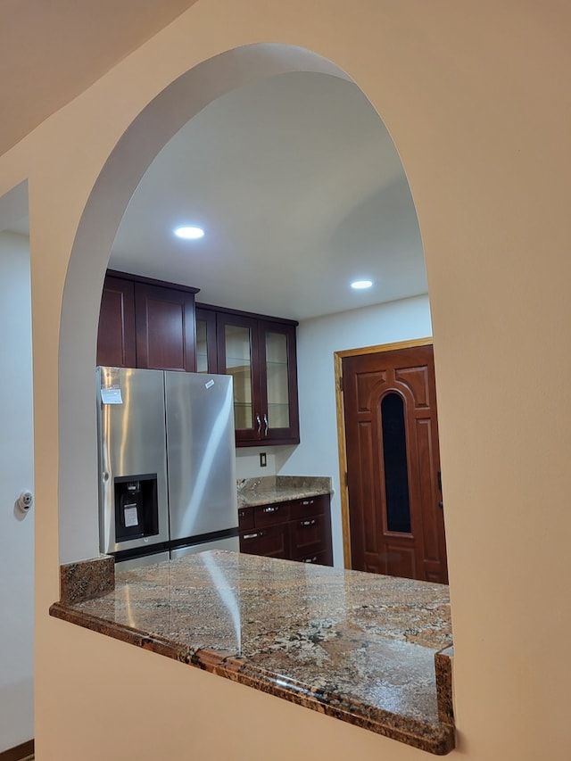 kitchen with stainless steel refrigerator with ice dispenser, dark stone countertops, and dark brown cabinetry