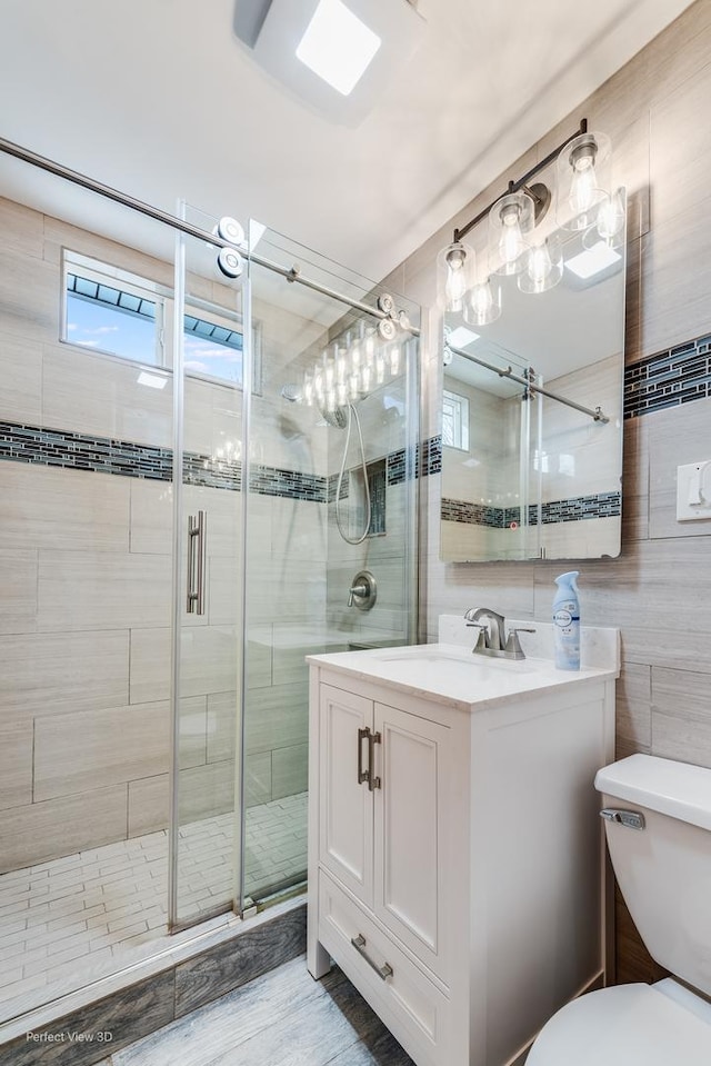 bathroom with tile walls, vanity, a shower with shower door, and toilet