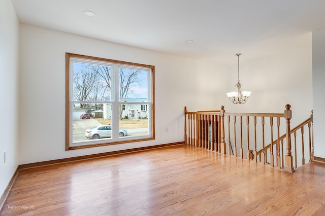 unfurnished room with light wood-type flooring and a notable chandelier