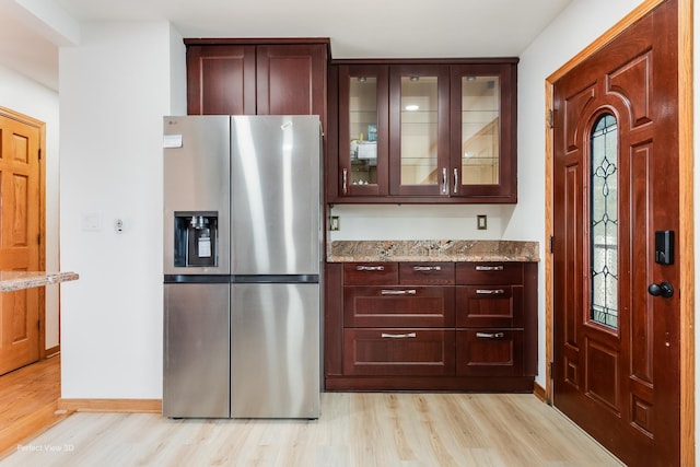 kitchen with light stone counters, light wood-type flooring, and stainless steel refrigerator with ice dispenser