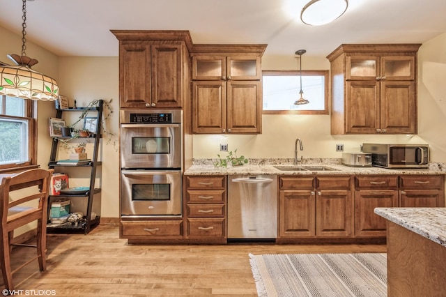 kitchen featuring appliances with stainless steel finishes, light hardwood / wood-style floors, pendant lighting, and light stone countertops