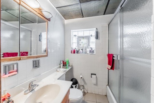 full bathroom featuring combined bath / shower with glass door, tile walls, vanity, toilet, and tile patterned floors