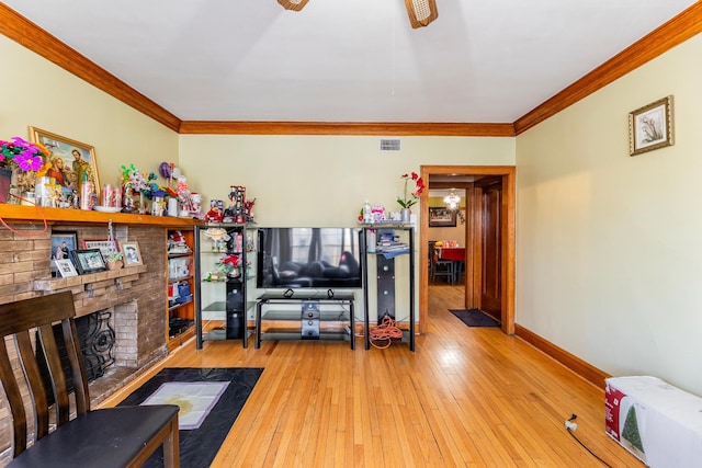 living room featuring crown molding, ceiling fan, a brick fireplace, and light wood-type flooring