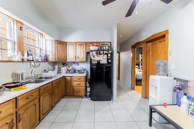 kitchen featuring sink, light tile patterned floors, ceiling fan, black refrigerator, and decorative backsplash