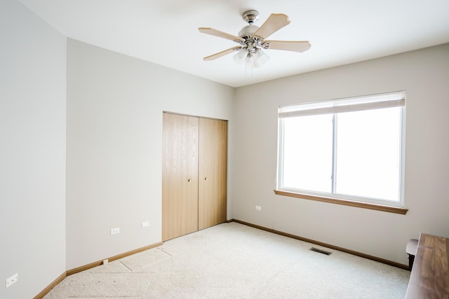 unfurnished bedroom featuring baseboards, visible vents, light colored carpet, ceiling fan, and a closet