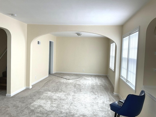 spare room featuring light colored carpet, visible vents, baseboards, and stairs