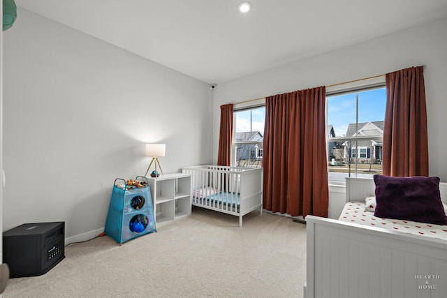 carpeted bedroom featuring a nursery area and baseboards