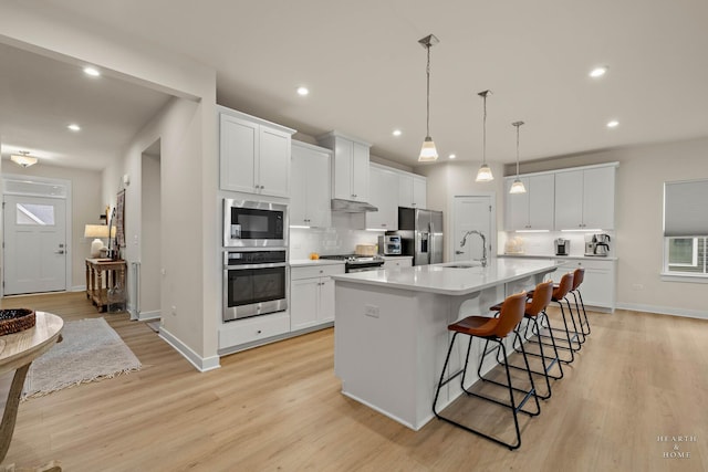 kitchen with light countertops, appliances with stainless steel finishes, a large island, tasteful backsplash, and a kitchen bar