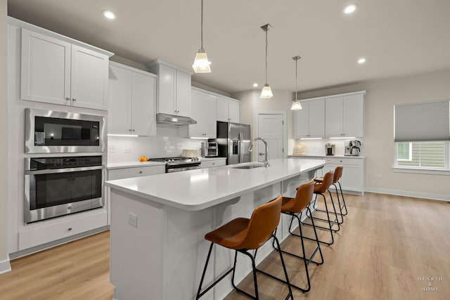 kitchen with under cabinet range hood, a sink, appliances with stainless steel finishes, a large island, and backsplash