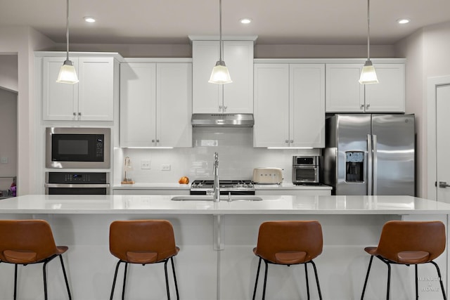 kitchen with white cabinets, decorative backsplash, appliances with stainless steel finishes, under cabinet range hood, and a kitchen bar