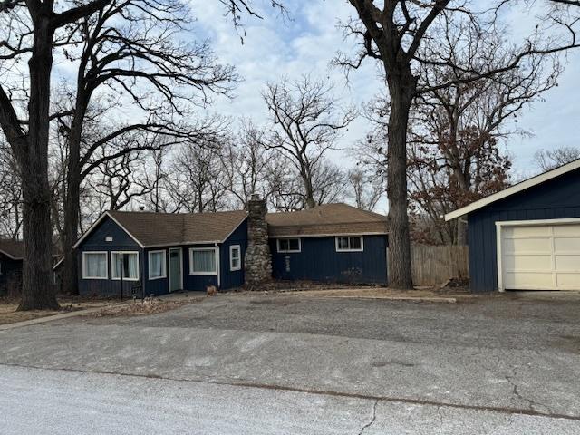 ranch-style house featuring a garage, a chimney, aphalt driveway, and board and batten siding