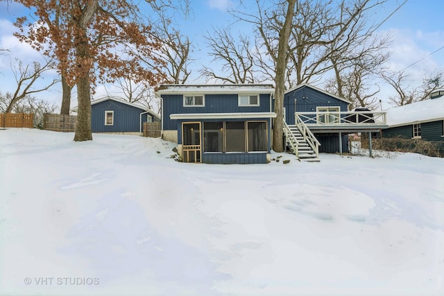 snow covered rear of property with a sunroom, stairs, and a deck