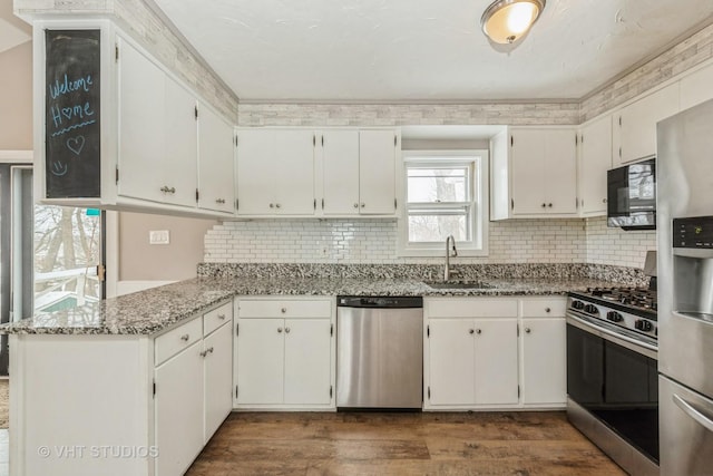 kitchen featuring stainless steel appliances, dark wood-type flooring, white cabinetry, a sink, and light stone countertops