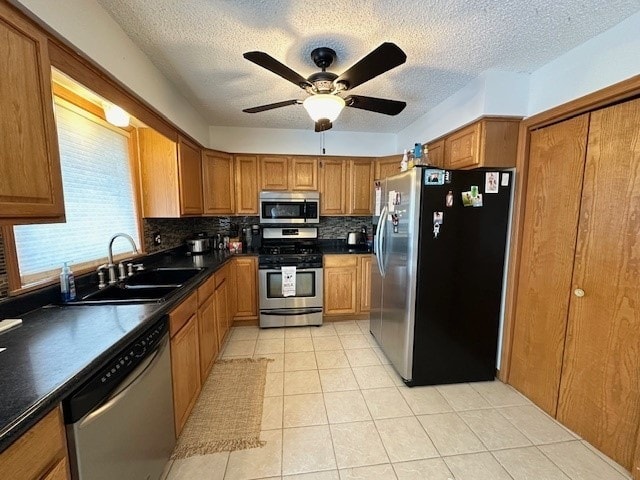 kitchen with sink, light tile patterned floors, appliances with stainless steel finishes, ceiling fan, and decorative backsplash