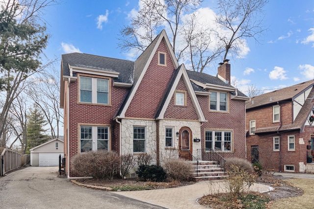 tudor home featuring an outbuilding, brick siding, a detached garage, a chimney, and stone siding