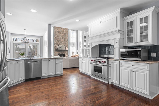 kitchen with appliances with stainless steel finishes, pendant lighting, white cabinets, and glass insert cabinets