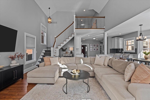 living room featuring visible vents, stairway, an inviting chandelier, wood finished floors, and high vaulted ceiling