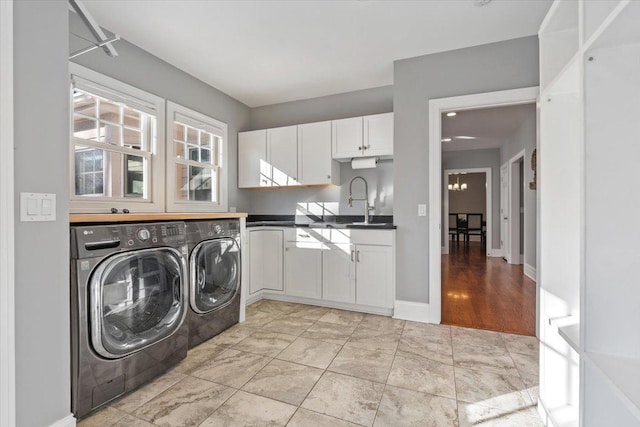 clothes washing area with cabinet space, baseboards, an inviting chandelier, washer and dryer, and a sink