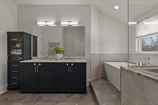 bathroom with tile walls, double vanity, vaulted ceiling, a sink, and a freestanding tub