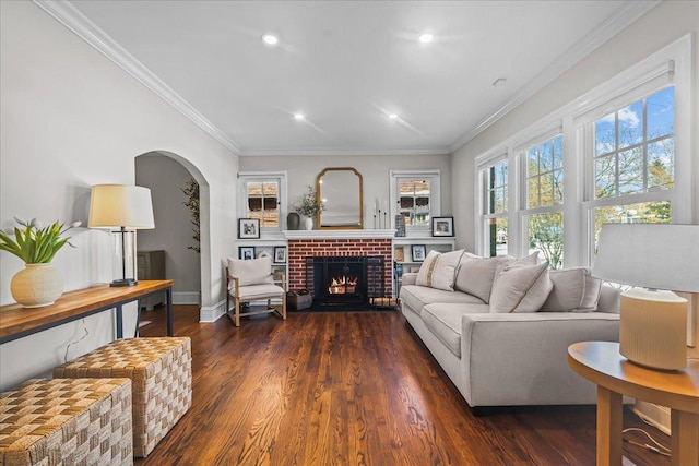 living area featuring arched walkways, dark wood-style flooring, a fireplace, baseboards, and ornamental molding