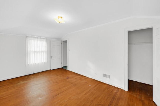 unfurnished bedroom featuring wood-type flooring, lofted ceiling, crown molding, and a closet