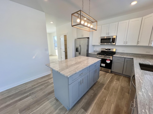 kitchen with white cabinetry, appliances with stainless steel finishes, a kitchen island, pendant lighting, and light stone countertops