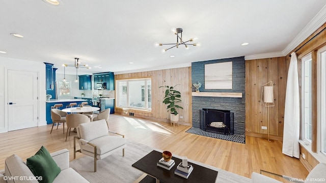 living room featuring light hardwood / wood-style flooring, crown molding, a stone fireplace, wooden walls, and a chandelier