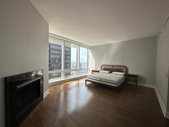 bedroom with dark wood-style floors, expansive windows, baseboards, and a city view