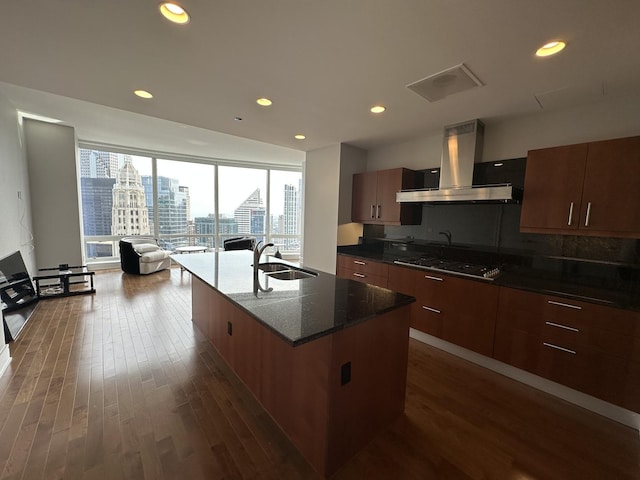 kitchen with a sink, exhaust hood, a view of city, an island with sink, and stainless steel gas stovetop