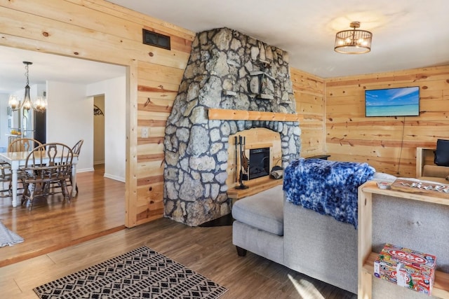 living room featuring wood-type flooring, wooden walls, a chandelier, and a stone fireplace